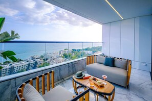 A modern balcony with a sofa, chairs, and a table set for two, overlooking a cityscape and the sea. - The Icon Limassol  (Limassol)