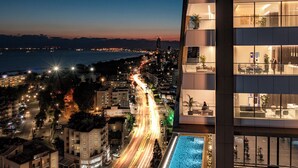Un hotel moderno con diversi balconi, una piscina e vista sulla città illuminata di notte.