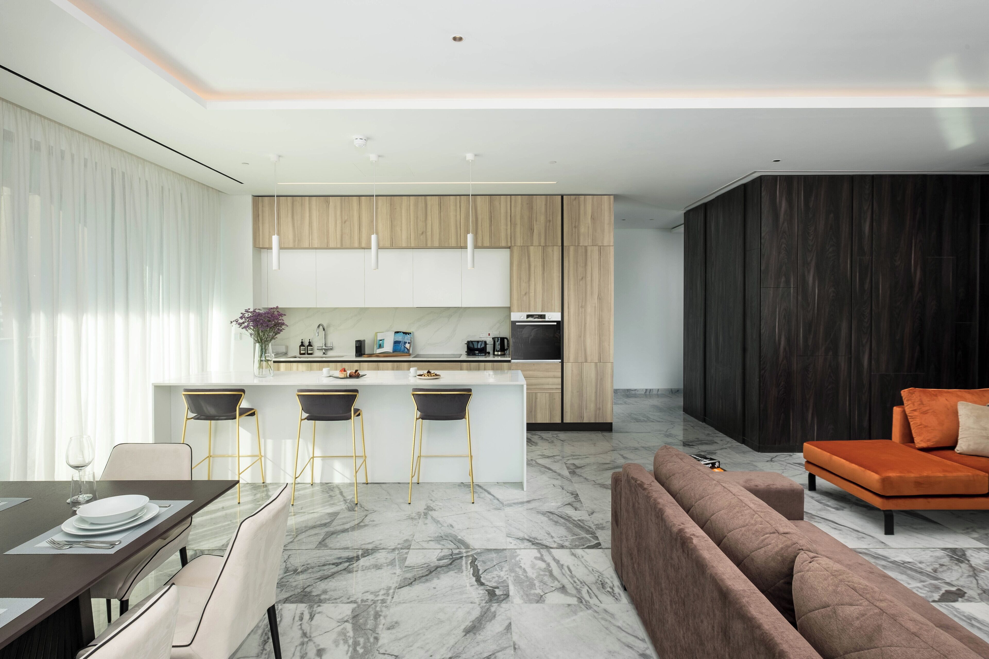 A modern kitchen with a central island, bar stools, and a dark wood accent wall.