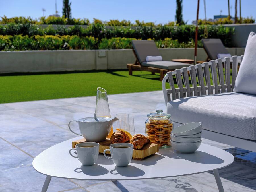 A breakfast setup with a coffee pot, cups, pastries, and a jar of cookies on a round table.