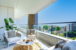 Een modern balkon met een witte bank, een rieten tafeltje en potplanten.
