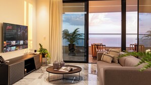 Un soggiorno moderno con un'ampia televisione, un tavolino da caffè e un divano. È presente un balcone con vista sull'oceano.