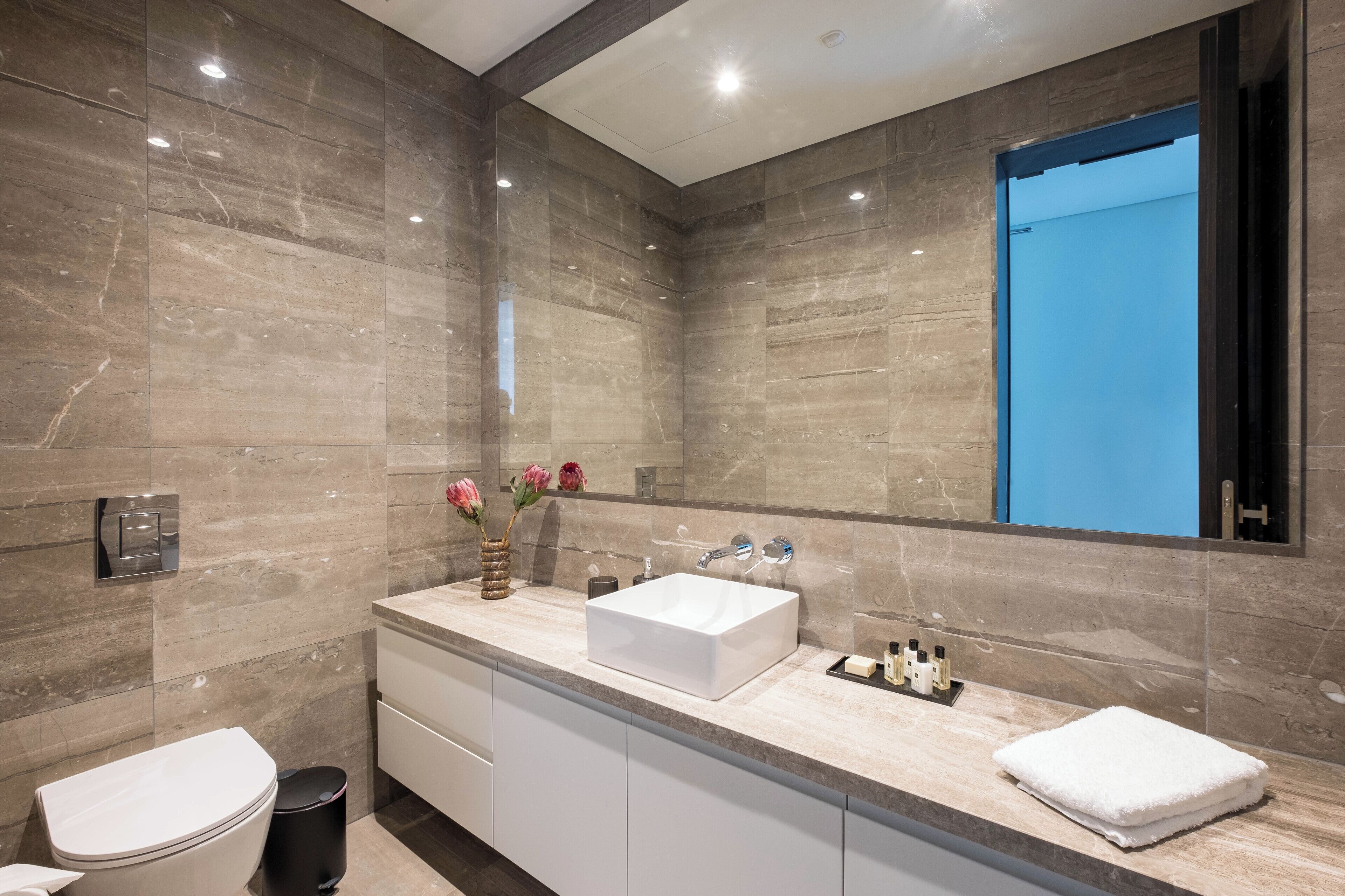 Une salle de bain moderne avec un grand miroir, un lavabo blanc et des toilettes.