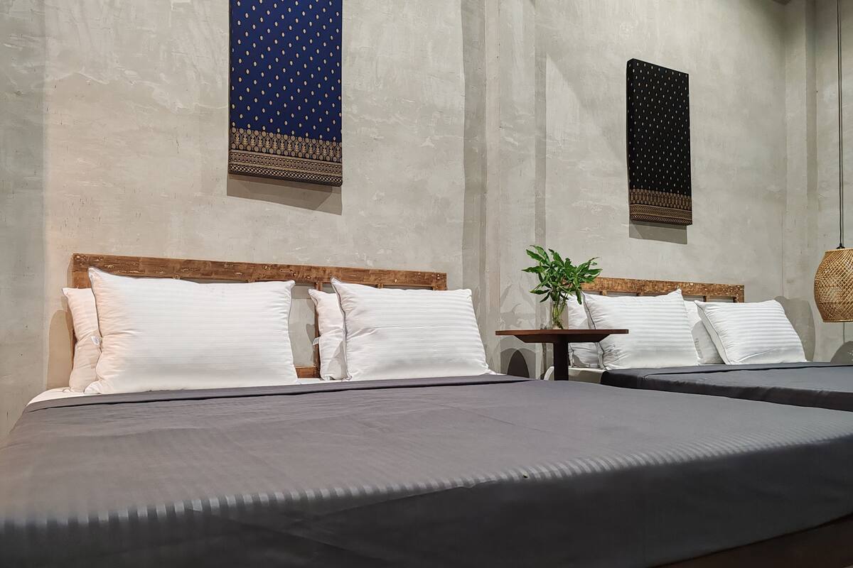 Une chambre d’hôtel avec deux lits, une petite table agrémentée d’une plante et deux éléments décoratifs fixés au mur.