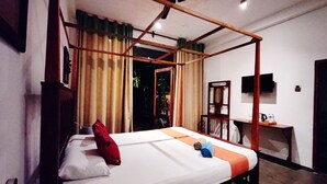 Een kamer met een bed, een bureau, een televisie en een plafondventilator.