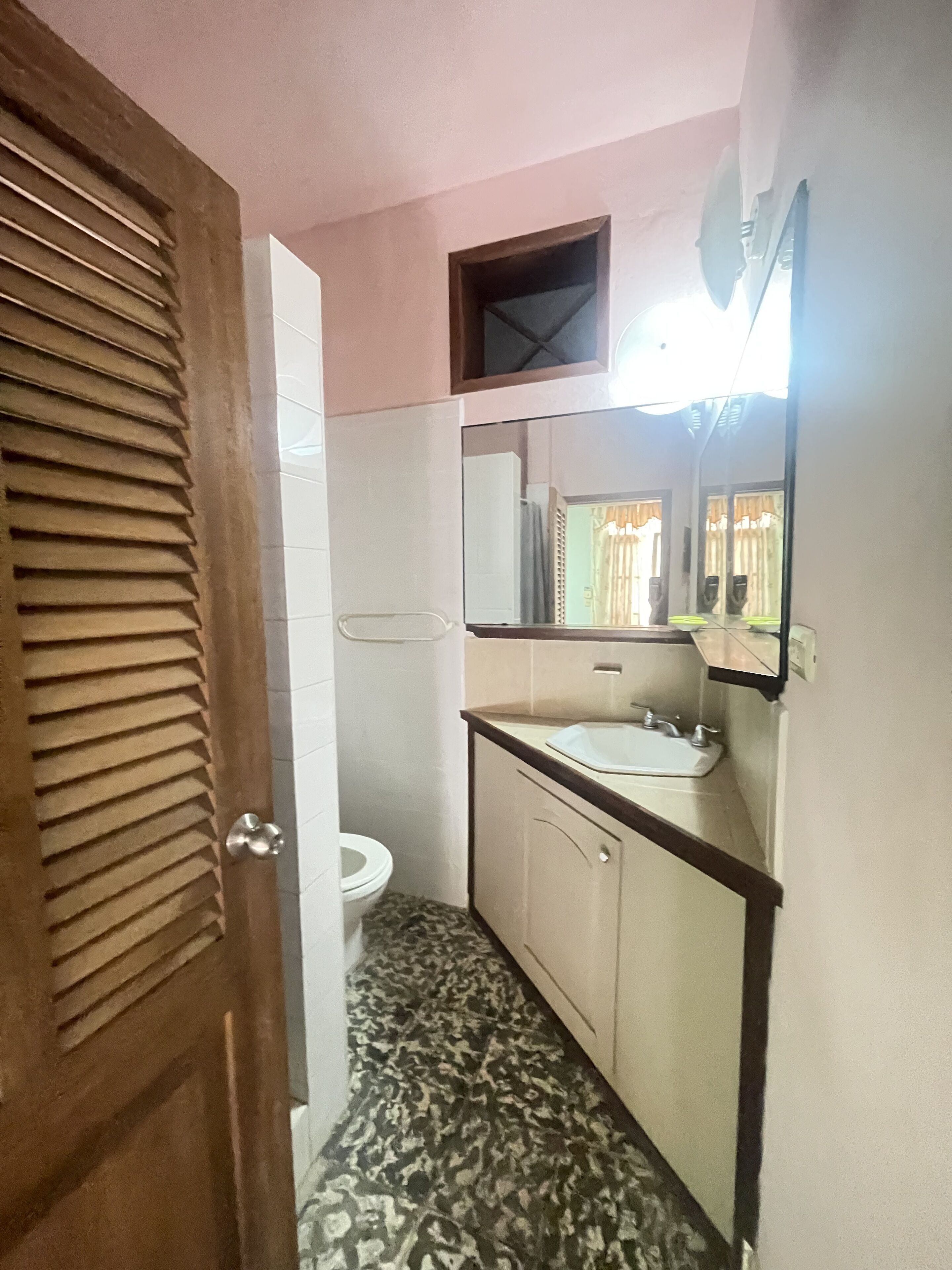 A bathroom with a toilet, sink, mirror, and patterned floor.