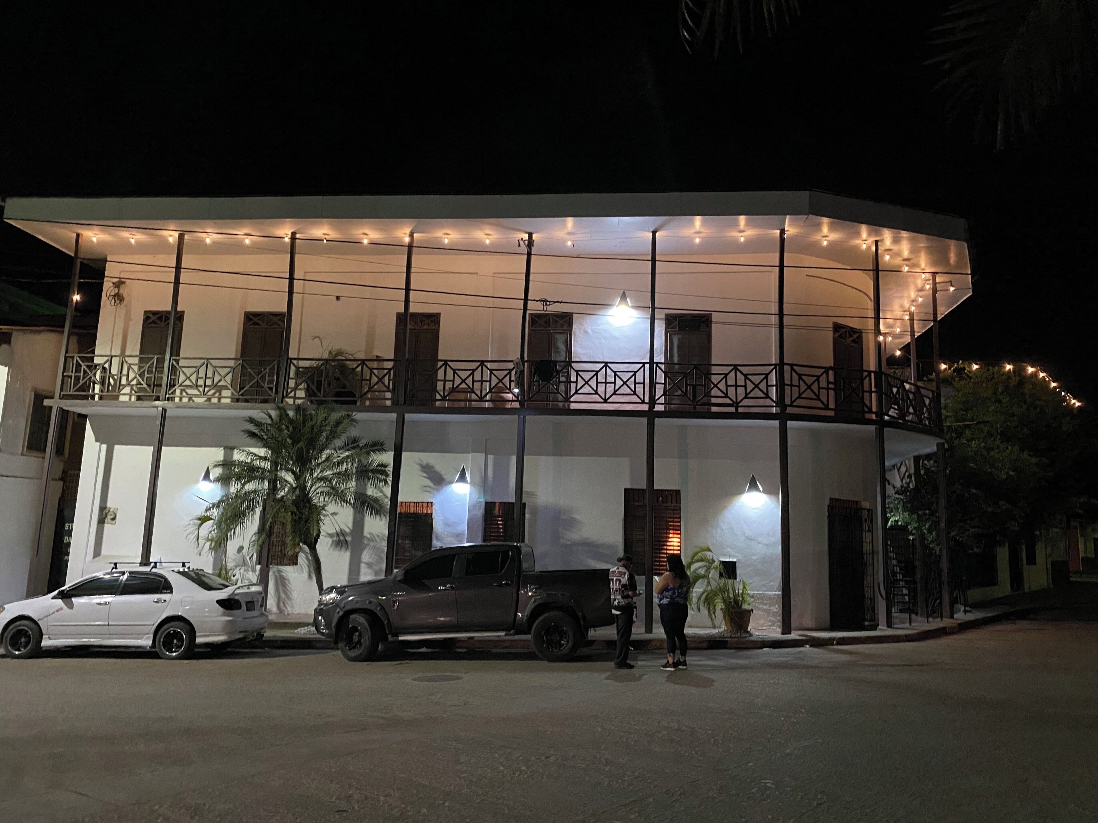 A two-story building with a balcony, string lights, and a parked car.