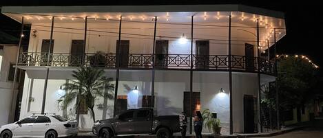 A two-story building with a balcony, string lights, and a parked car.
