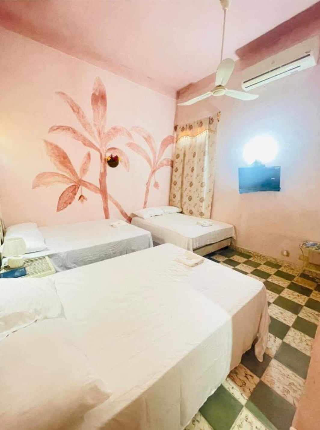 A room with two single beds, a ceiling fan, an air conditioner, a patterned wall mural, and a checkered floor.