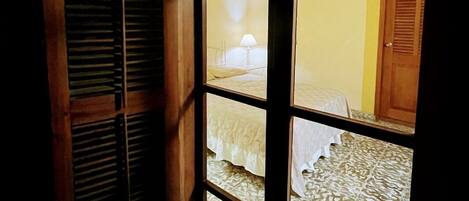 A room with a large window, wooden shutters, and a bed with patterned bedding.