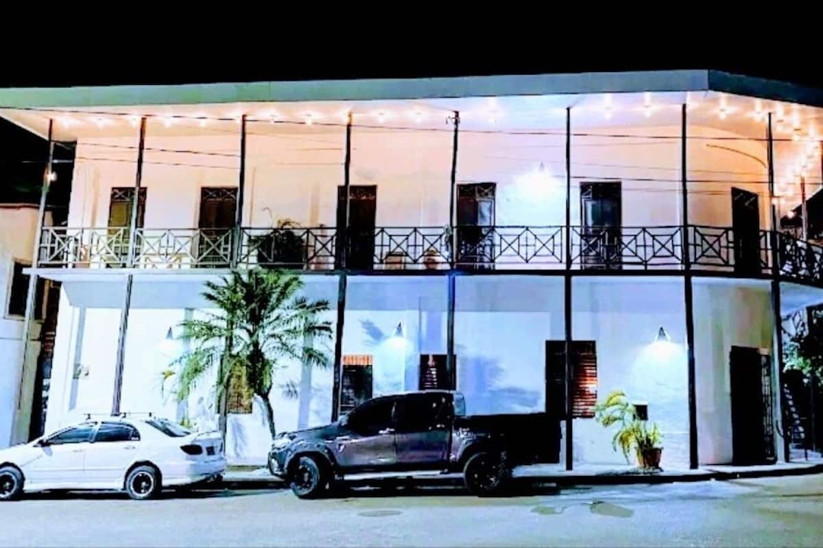 A modern building with a balcony, a car parked in front, and a palm tree nearby.