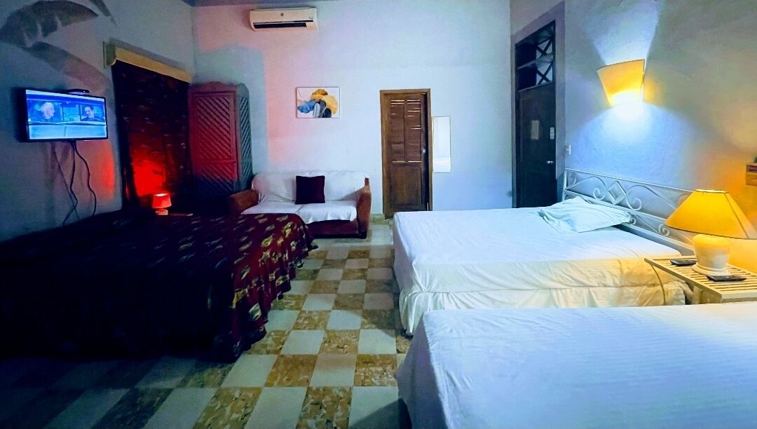 A hotel room with two beds, a TV, a red curtain, a painting, and a checkered floor.