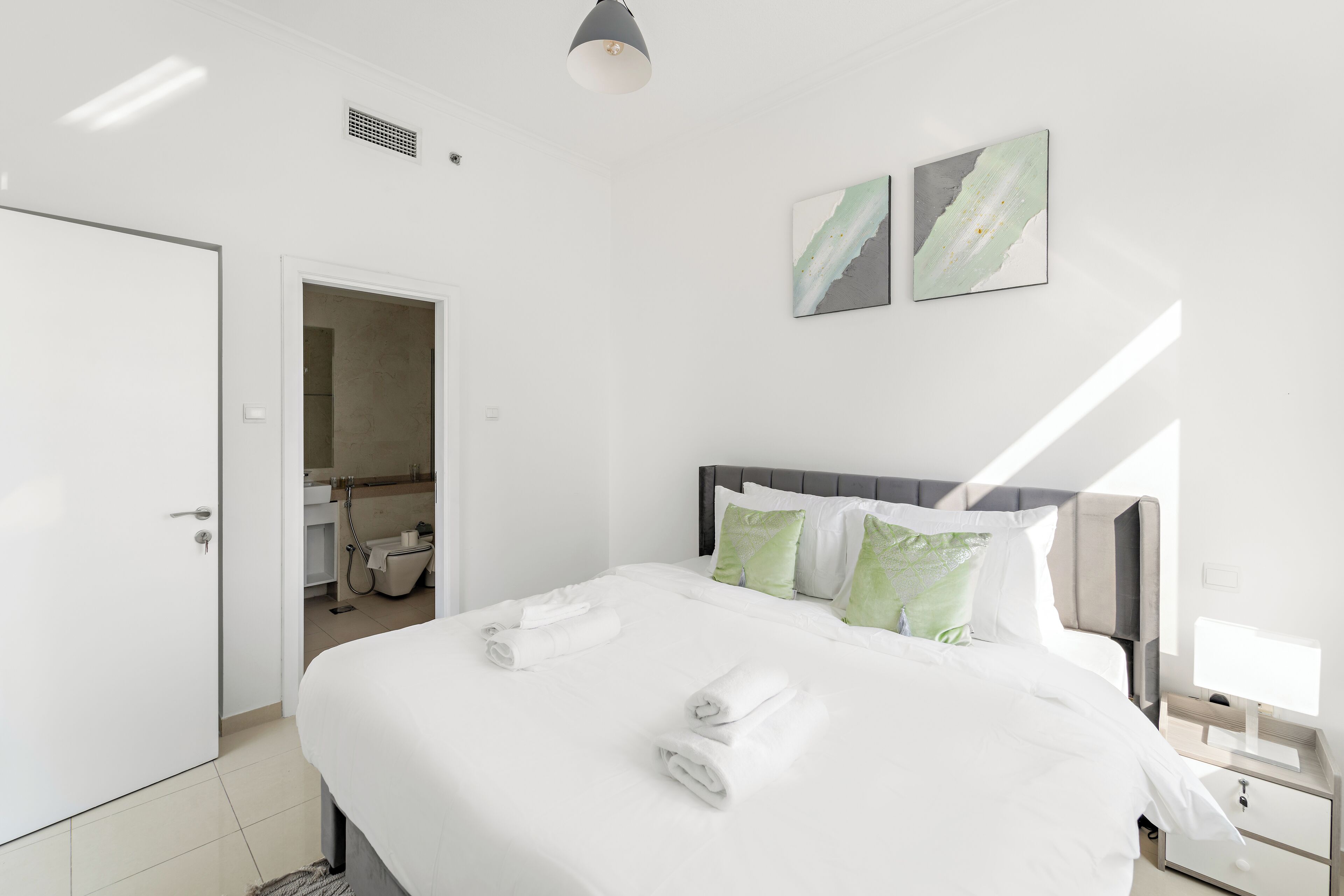 Une chambre d’hôtel moderne, dotée d’un grand lit, d’une table de chevet, d’une petite table et d’une fenêtre laissant entrer la lumière naturelle.
