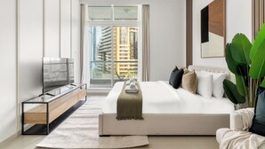 A modern bedroom with a large bed, a TV on a glass cabinet, and a view of tall buildings through the window. - Silkhaus Botanica Tower, Dubai Marina (Dubai)