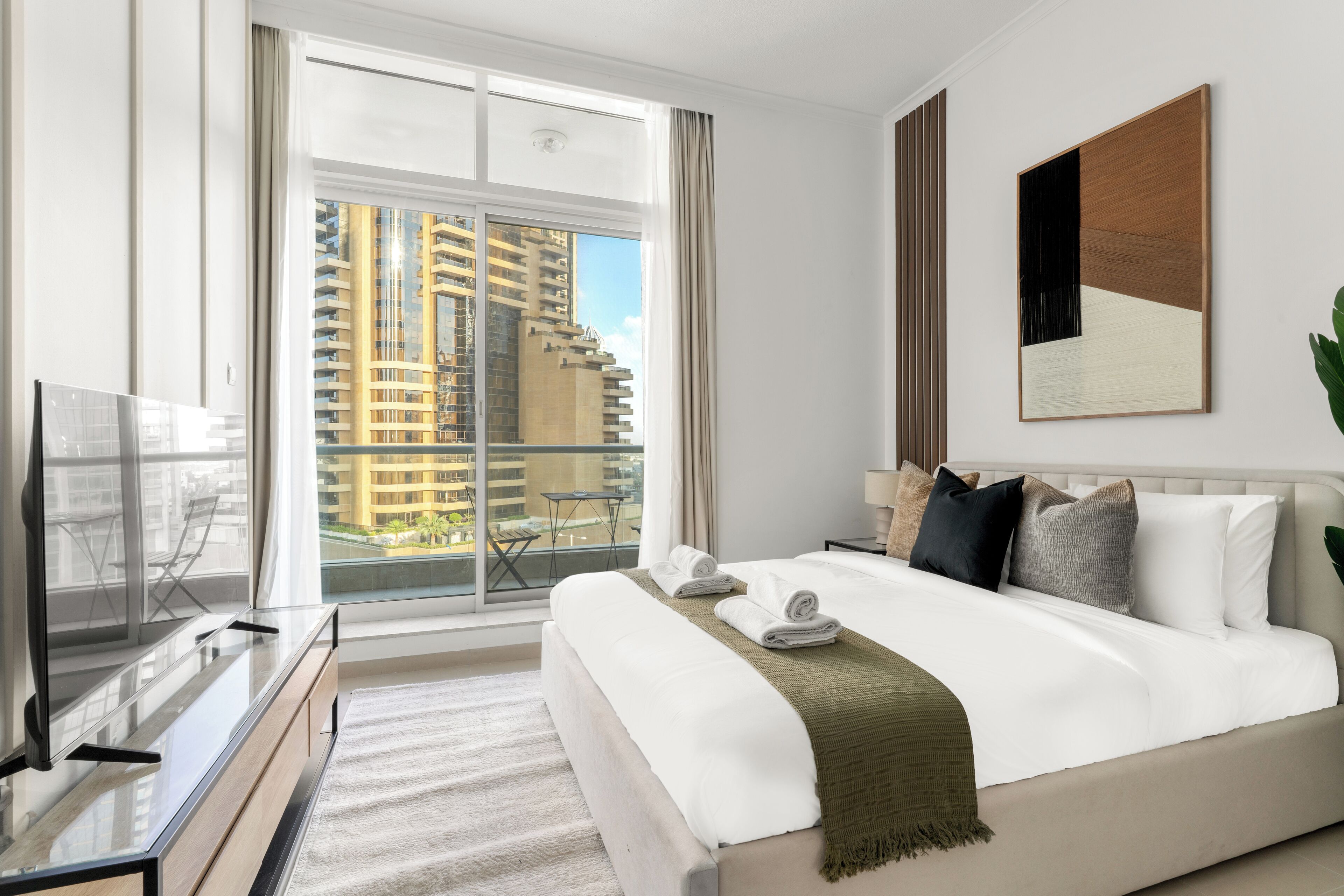 A modern hotel room with a large bed, a flat-screen TV, and a balcony with a city view.