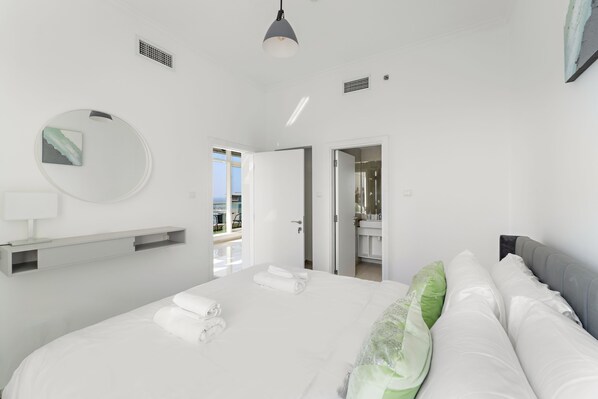 A modern hotel room with a large bed, a round mirror, a bedside table, and a view of the balcony.