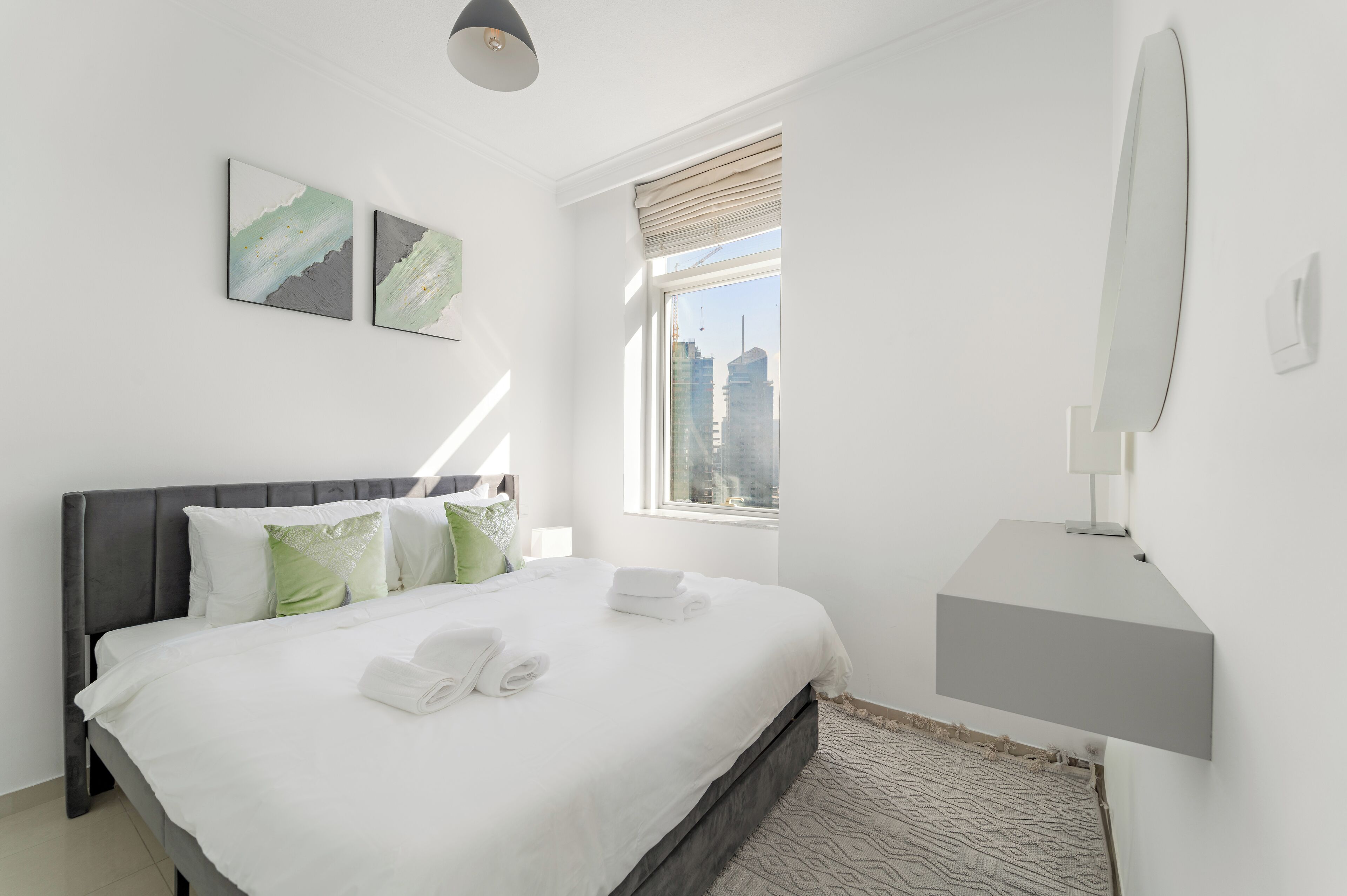 A modern hotel room with a large bed, a bedside table, a wall-mounted lamp, and two abstract paintings.