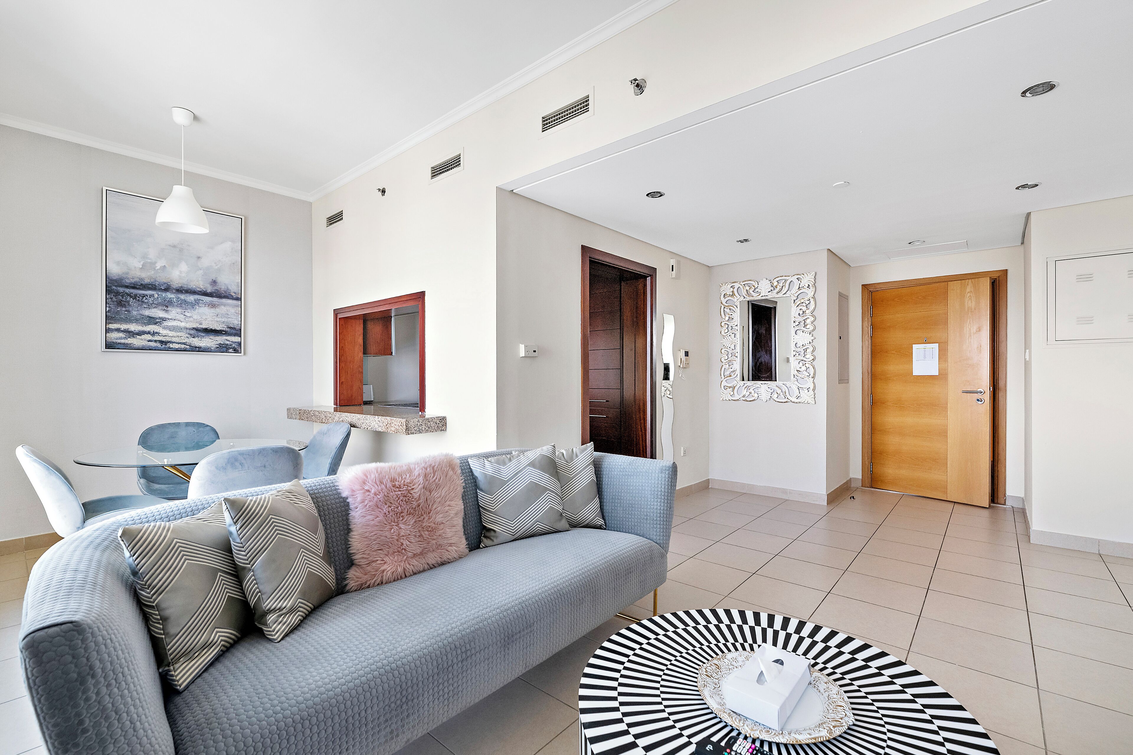 A modern living room with a grey sofa, a round coffee table, and a dining area with a blue chair and a small table.