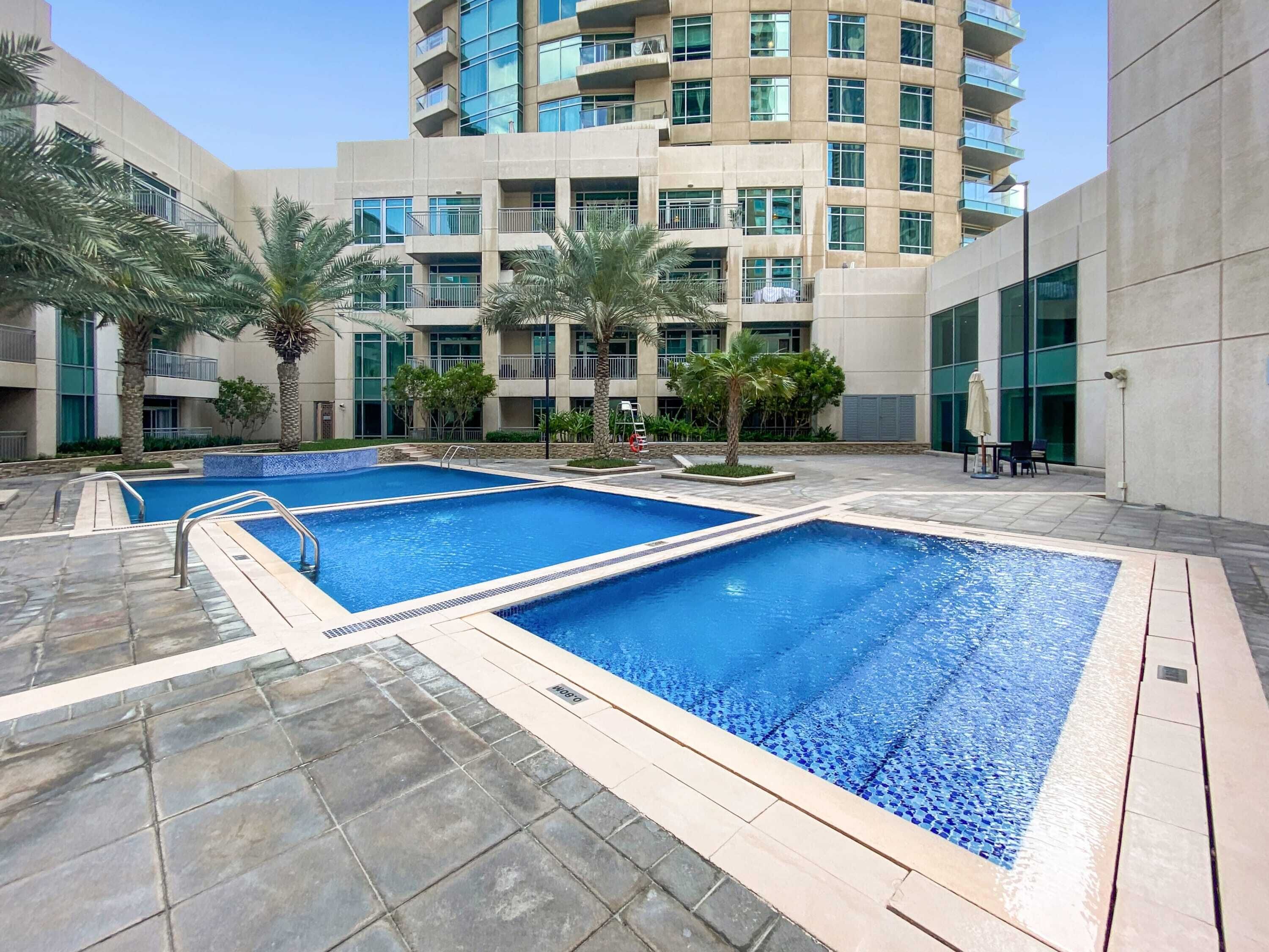 A modern building with a pool area, featuring two rectangular pools with tiled edges and a stone floor.