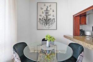 A modern dining area with a glass table, two chairs, a vase with flowers, and a chandelier. - Silkhaus Burj Views, Downtown Dubai (Dubai)