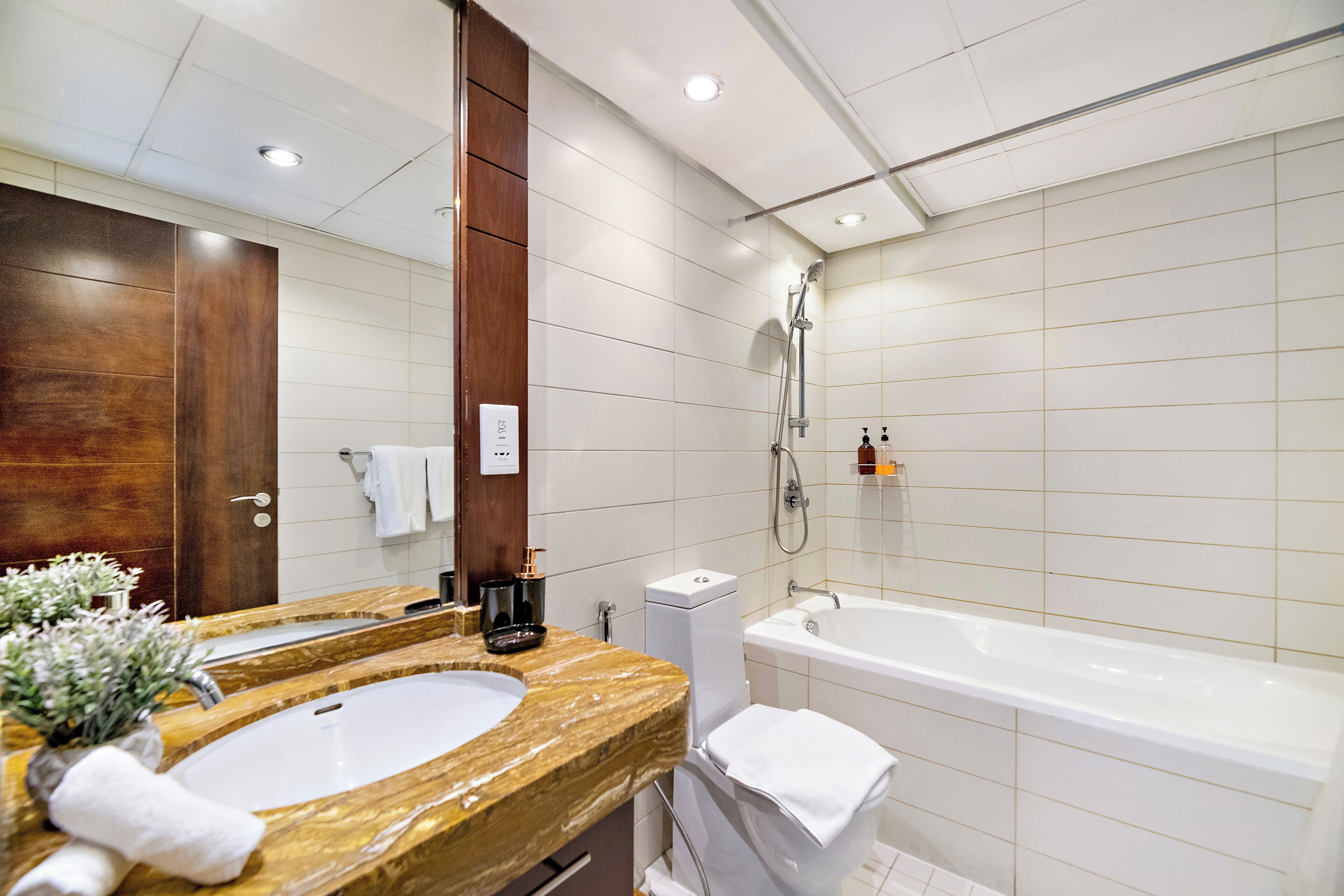 Un baño moderno con lavamanos de mármol, un espejo grande, una bañera y una ducha.
