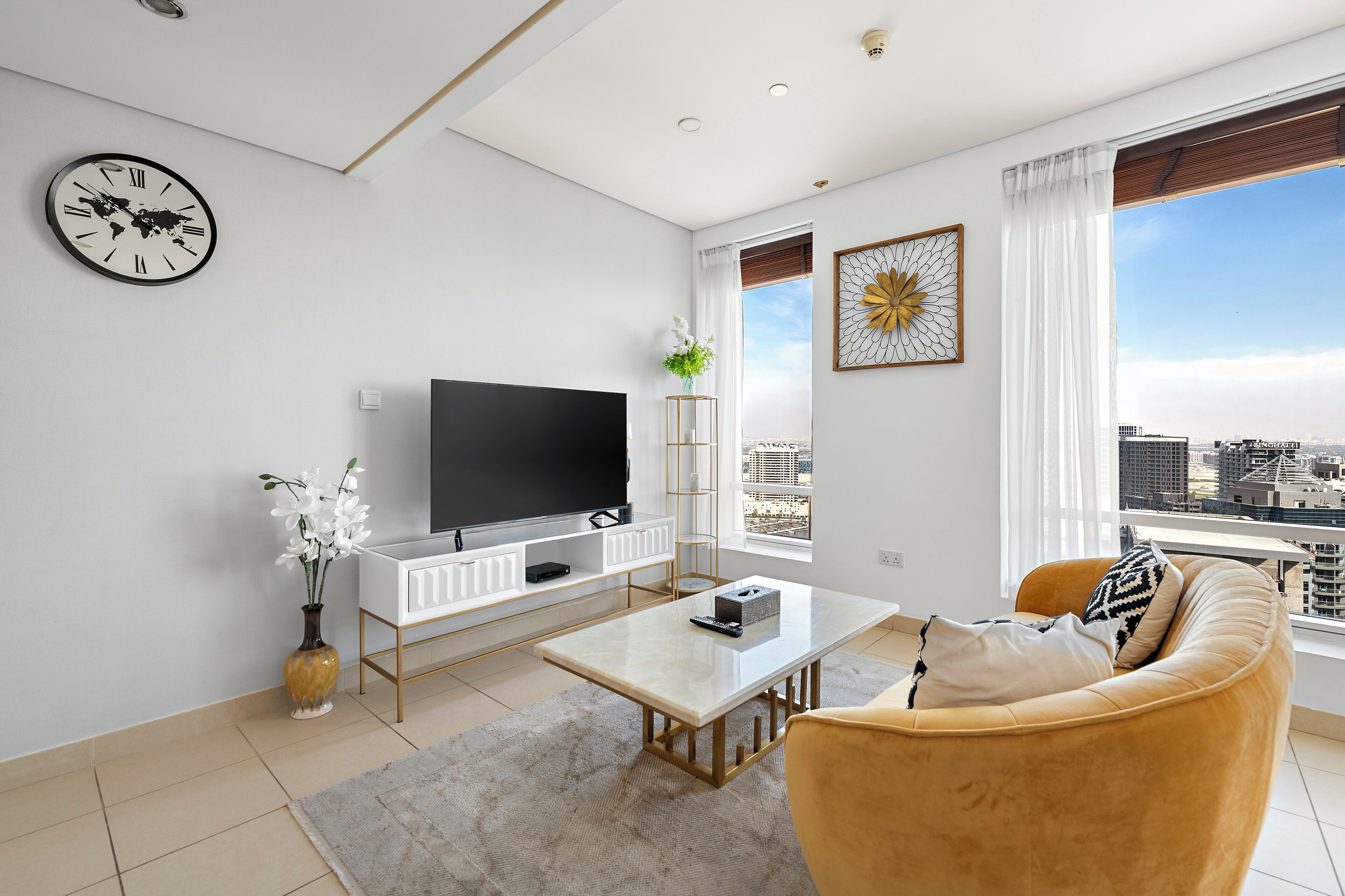 Een moderne woonkamer met een flatscreen televisie, een salontafel, een bank en een wereldkaartklok, met grote ramen met uitzicht op de stad.
