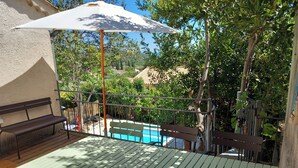 Une terrasse avec une piscine, des bancs en bois et un parasol.
