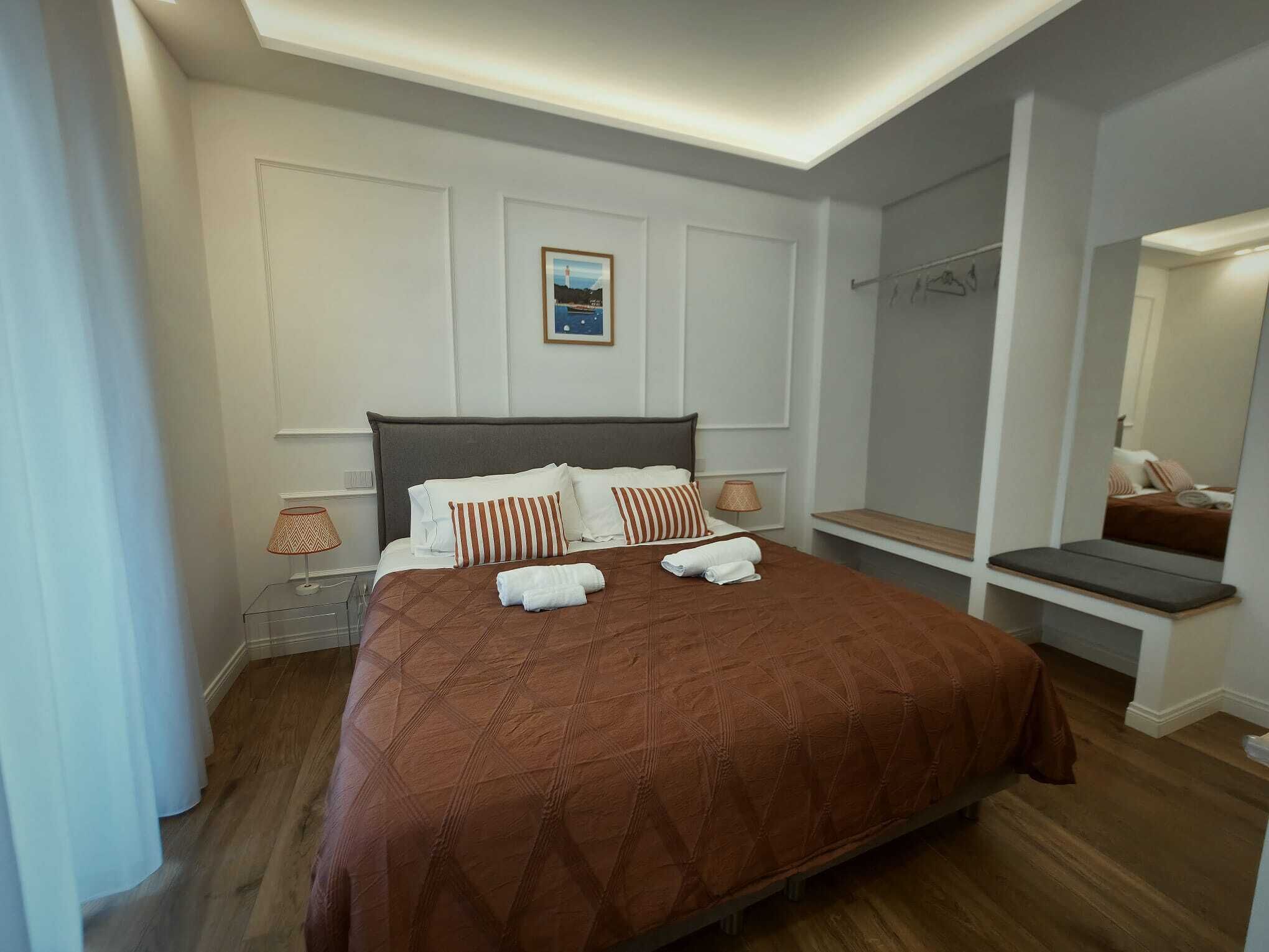 Een netjes ingerichte hotelkamer met een groot bed, nachtlampen, een klein bankje en een spiegel.