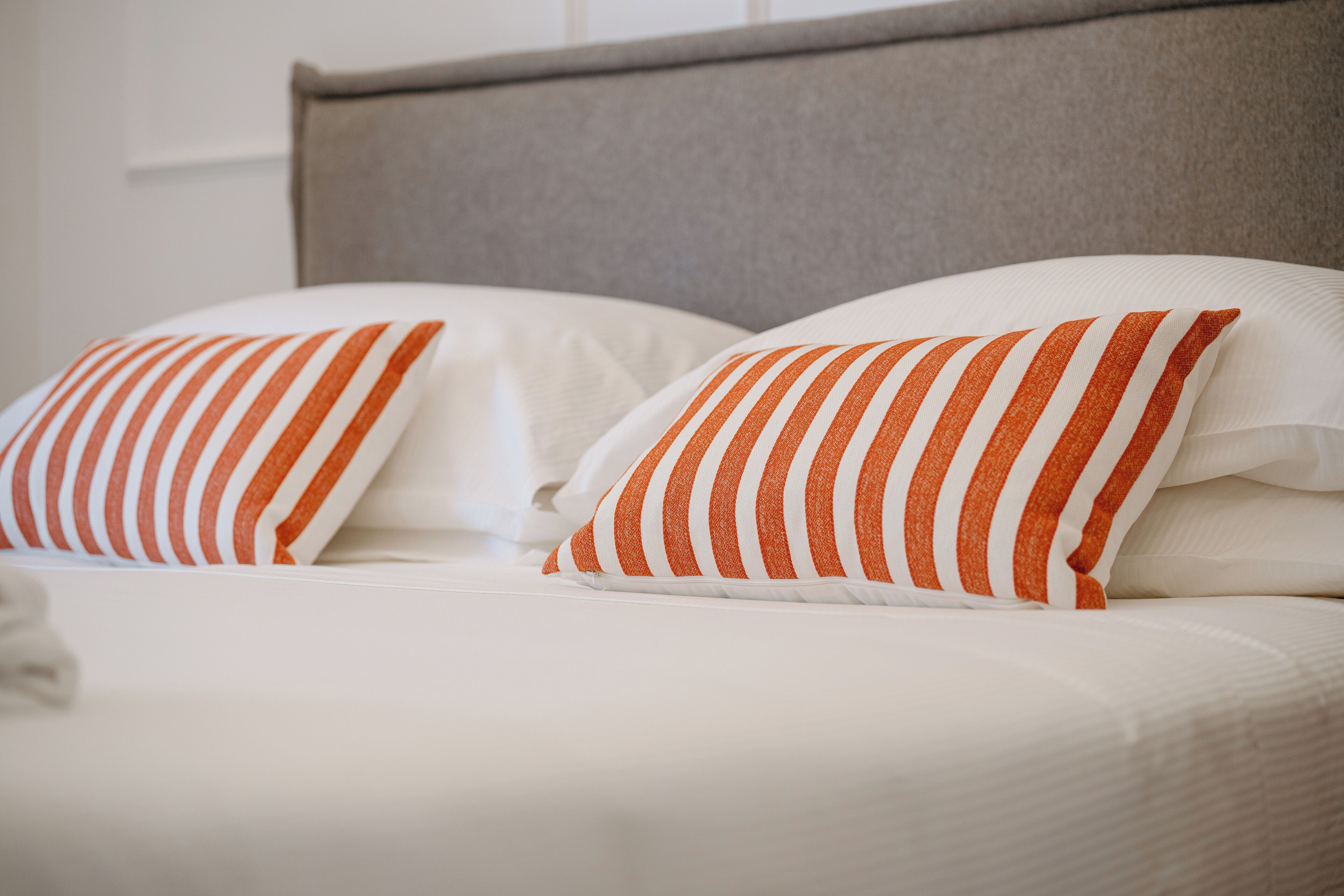 Uma cama com roupa de cama branca e almofadas listradas de laranja.