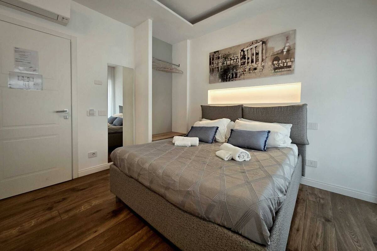 Un dormitorio con una cama grande, cabecera con iluminación integrada, un espejo y una obra de arte colgada en la pared.