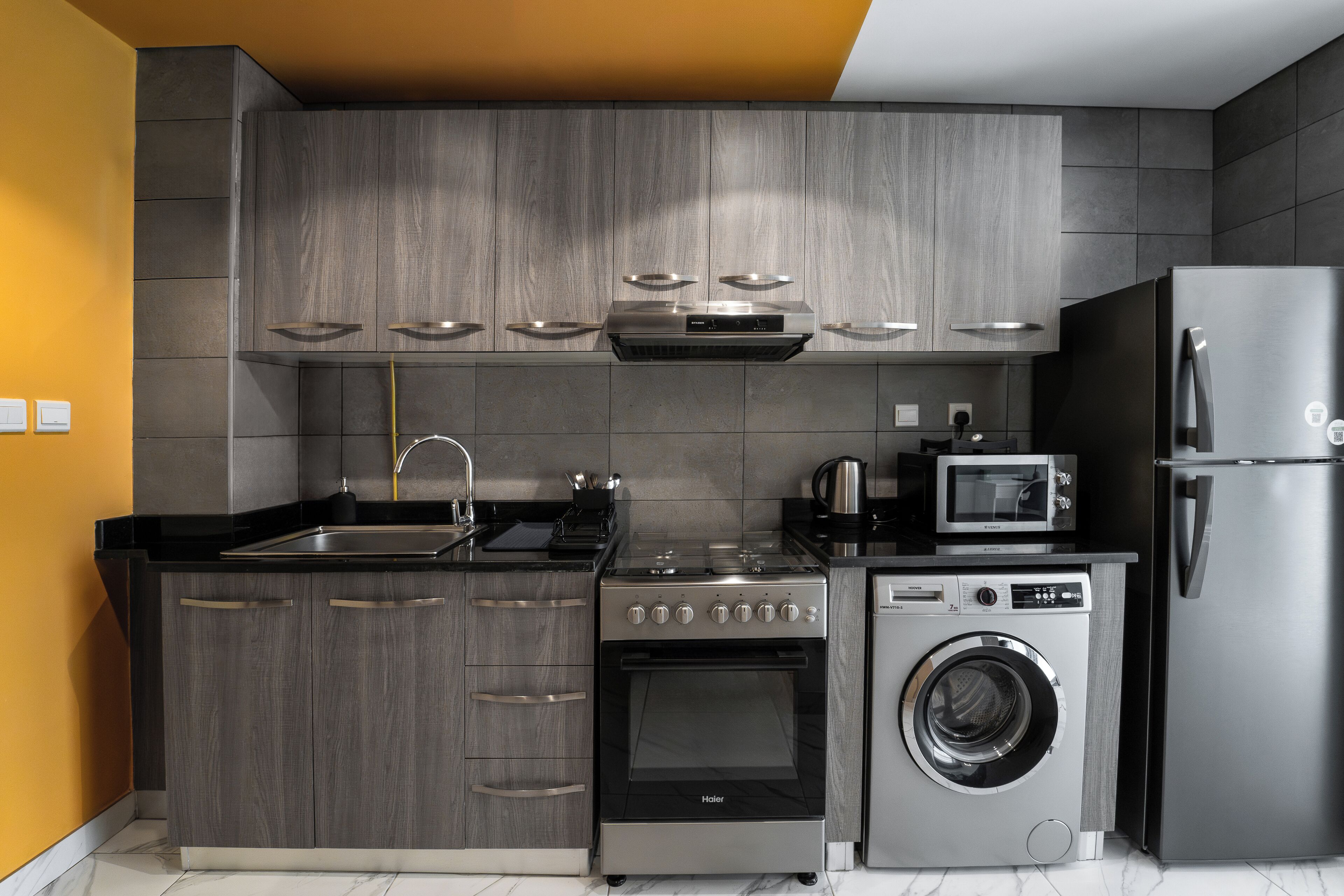 Une cuisine moderne avec des meubles de couleur grise, un four encastré, un four à micro-ondes, un lave-linge et un réfrigérateur en acier inoxydable.