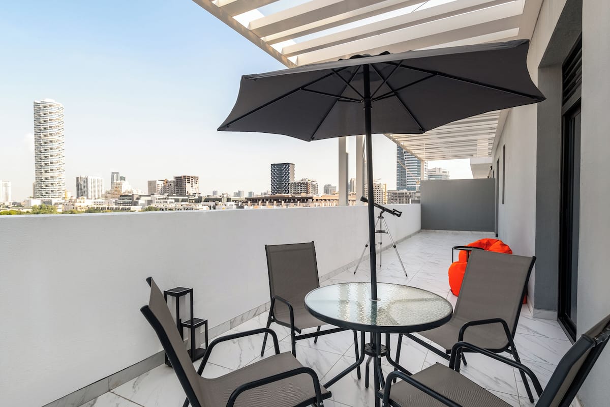 A balcony with a glass table and chairs, a large umbrella, and a city view.