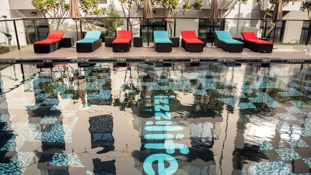 A swimming pool with lounge chairs and a glass barrier. - izzzi life Mint Holiday Home Apartments (Dubai)