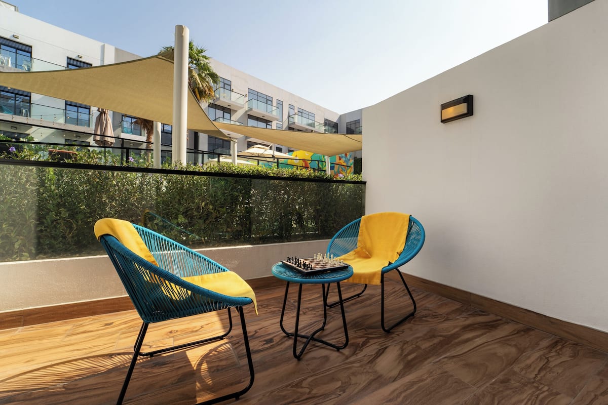 A balcony with two chairs, a chessboard, and a view of a modern building.