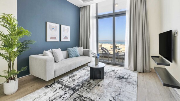 Ein modernes Wohnzimmer mit einer Couch, einem Couchtisch und einem großen Fenster mit Blick auf den Strand.