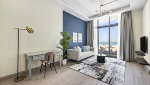 Ein modernes Wohnzimmer mit Schreibtisch, Stuhl, Sofa und großen Fenstern mit Blick ins Freie.
