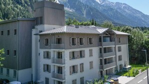 A multi-story building with balconies, set against a backdrop of snow-capped mountains.