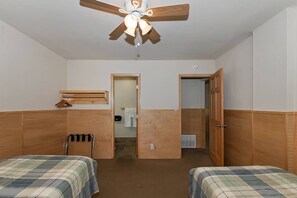 Ein Hotelzimmer mit zwei Betten, einem Deckenventilator, einem Holzschrank und einem durch eine geöffnete Tür einsehbaren Badezimmer.