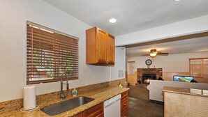 Una cocina con encimeras de granito, armarios de madera, lavavajillas y una ventana con persianas.