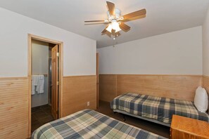Ein Zimmer mit zwei Betten, einem Deckenventilator und einer Holztür zu einem Badezimmer.