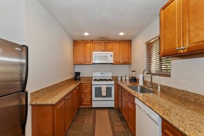 A compact kitchen with wooden cabinets, a stainless steel refrigerator, a microwave, an oven, and a dishwasher.