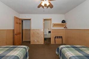 Ein Schlafzimmer mit zwei Betten, einem Deckenventilator, einer Holztür und einem kleinen Regal mit einem Ventilator.