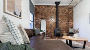 A modern living room with a brown leather sofa, a round wooden coffee table, and a brick wall with a black chimney.