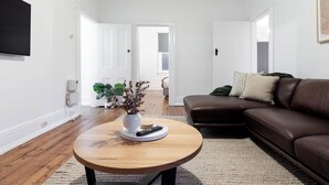 A modern living room with a wooden coffee table, a brown leather sofa, and a white wall-mounted TV.