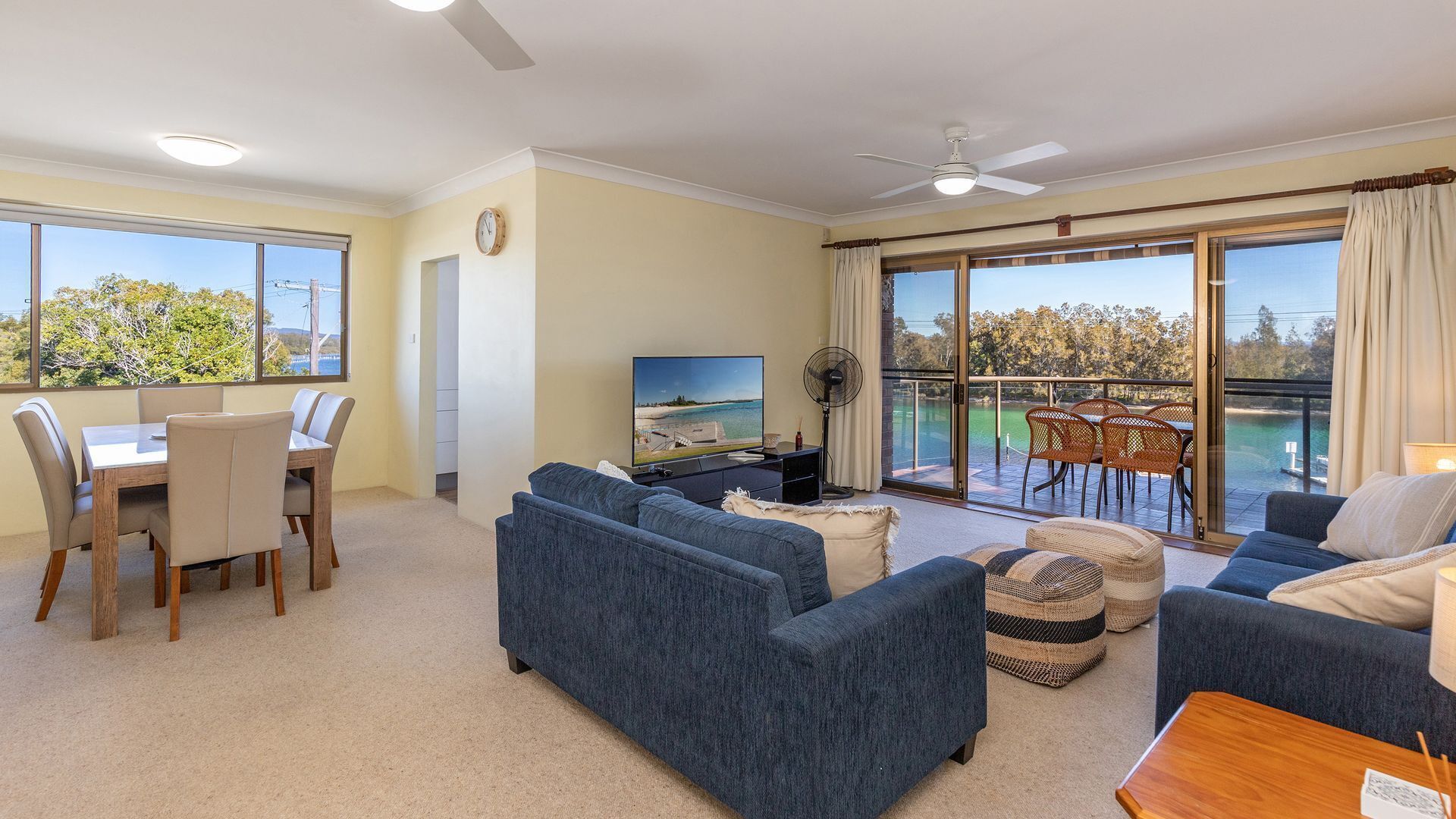 A spacious living area with a balcony, a dining set, and a television.