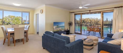 A spacious living area with a balcony, a dining set, and a television.