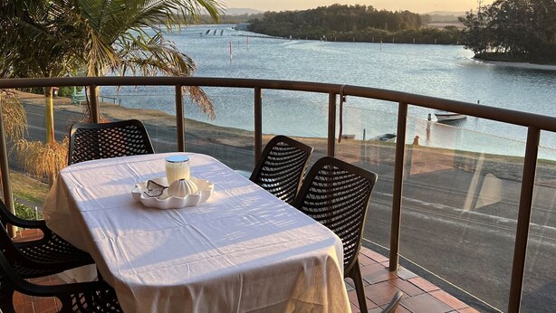 A balcony with a table set for two, overlooking a river. - Braemar 7 - Lakefront apartment (Forster)