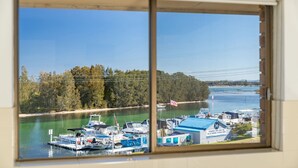 A marina with boats docked, a flag, and a building with a sign indicating services like ice cream and snacks. - Braemar 7 - Lakefront apartment (Forster)
