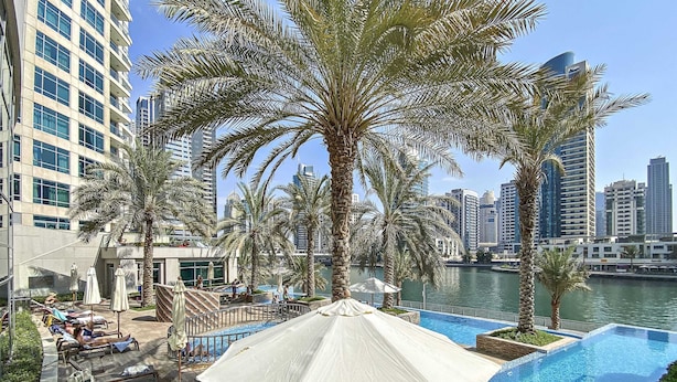 A poolside area with lounge chairs, umbrellas, and a view of the city skyline.