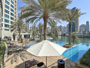 A poolside area with lounge chairs, umbrellas, and a view of the city skyline. - Silkhaus Fairfield, Dubai Marina (Dubai)